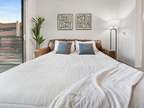 A bedroom with a large bed, two pillows, a bedside lamp, and a wall-mounted artwork.