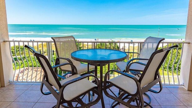 A balcony with a round table and chairs, overlooking a beach. - 3BR Oceanfront Condo w/ Direct Beach Access & Pool (Holmes Beach)