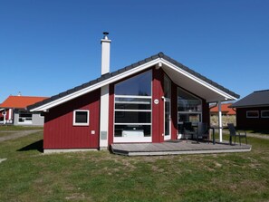 Ein modernes, rotes Gebäude mit einem großen Glasfenster, einem Schornstein und einer kleinen Veranda mit Stühlen.