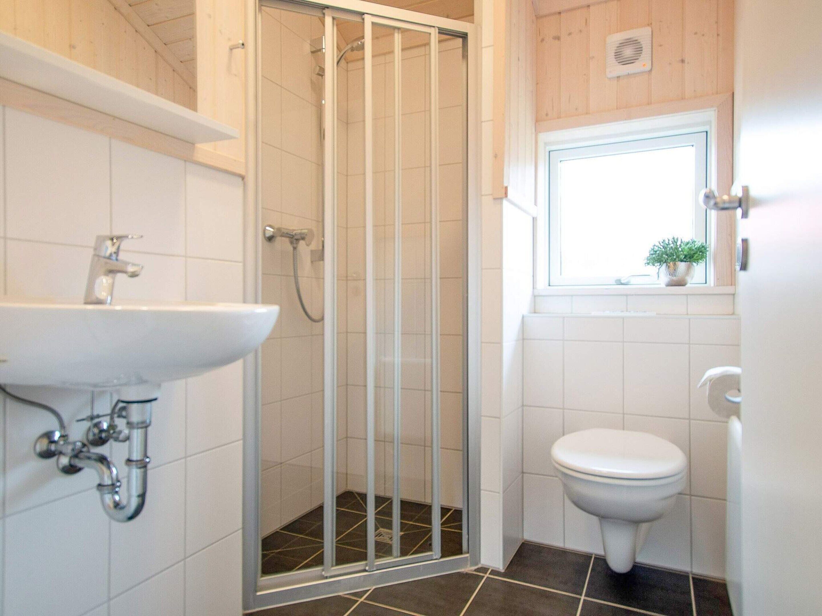 A bathroom with a shower enclosure, a sink, a toilet, and a window with a plant.