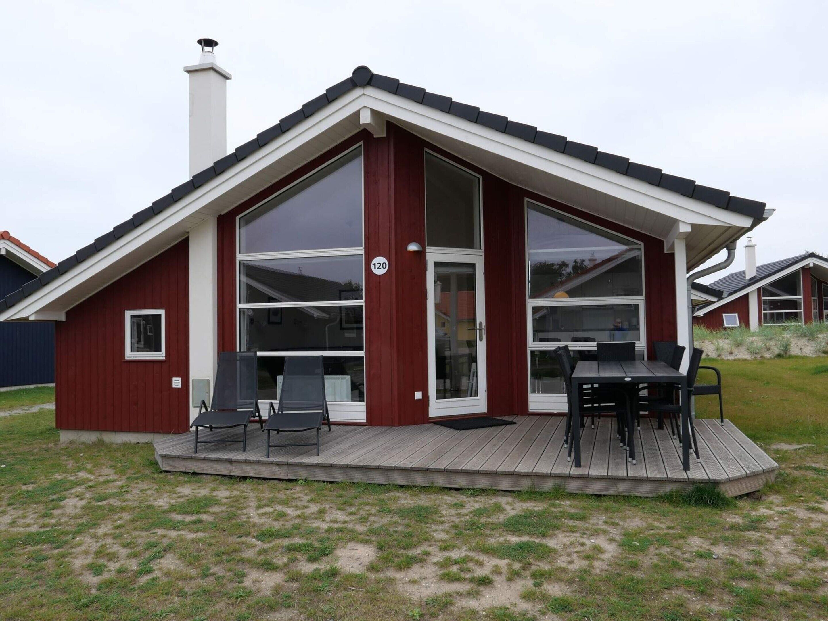 Ett modernt hus med en veranda, stora fönster och en skorsten.