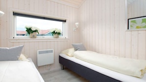 Ein Zimmer mit zwei Betten, einem Fenster mit Pflanzen, einem Wandheizkörper und einem Spiegel.