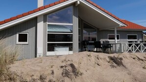 Ein Strandhaus mit rotem Dach, großen Fenstern und einer überdachten Terrasse.