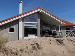 A beach house with a red roof, large windows, and a covered patio area. - Nordic-style Sanctuary With Sauna (Grossenbrode)