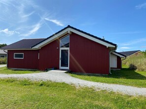 A red single-story building with a white door and window, a gravel driveway, and a clear blue sky. - Pet-friendly Coastal Base (Grossenbrode)