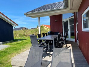 A covered patio with a table and chairs, a grill, and a view of a red building. - Pet-friendly Coastal Base (Grossenbrode)