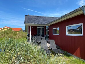 A red building with a grey roof, a covered porch with chairs, and a window. - Pet-friendly Coastal Base (Grossenbrode)