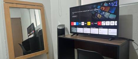 Ein kleiner, sauberer Raum mit Schreibtisch, Computer, Stuhl, Mülleimer und Spiegel.