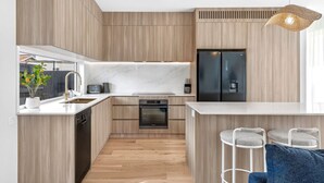 Een moderne keuken met houten keukenkastjes, een inbouwoven, een koelkast en een bar met barkrukken.