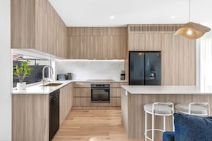 Een moderne keuken met houten keukenkastjes, een inbouwoven, een koelkast en een bar met barkrukken.