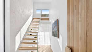 Een trap met houten treden en witte leuningen die leidt naar een kamer met een raam en een schilderij aan de muur.