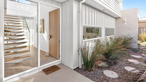 Een modern huis met een glazen deur, een houten deur en een kleine tuin met planten en een pad van stenen.
