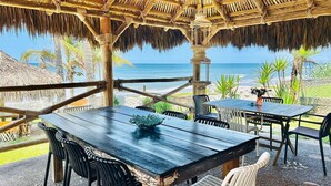 An outdoor dining area with tables and chairs, a thatched roof, and a view of the ocean. - Beach & Pool Getaway by a Partner Host (Celestino Gazca Villaseñor)