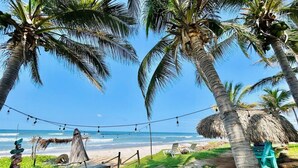 A beach with palm trees, a thatched structure, and a signpost with various destinations. - Beach & Pool Getaway by a Partner Host (Celestino Gazca Villaseñor)