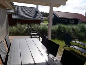 A covered outdoor area with a table and chairs, surrounded by greenery and a building with a tiled roof. - 4 Star Holiday Home in Grossenbrode (Grossenbrode)