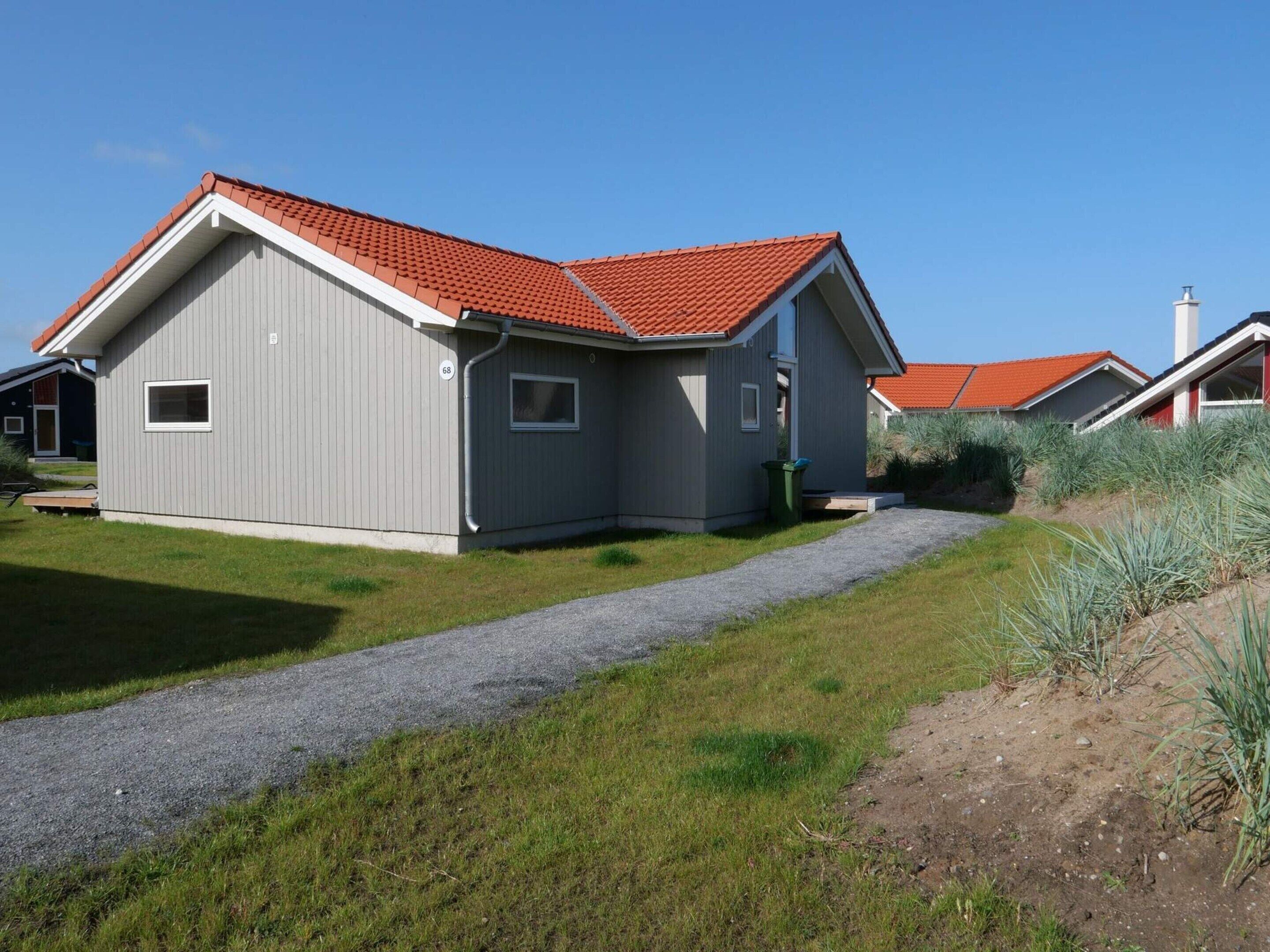A modern two-story house with a red-tiled roof, a gravel driveway, and a grassy yard.
