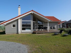 A modern house with a large glass window, a deck with outdoor furniture, and a red-tiled roof. - 4 Star Holiday Home in Grossenbrode (Grossenbrode)