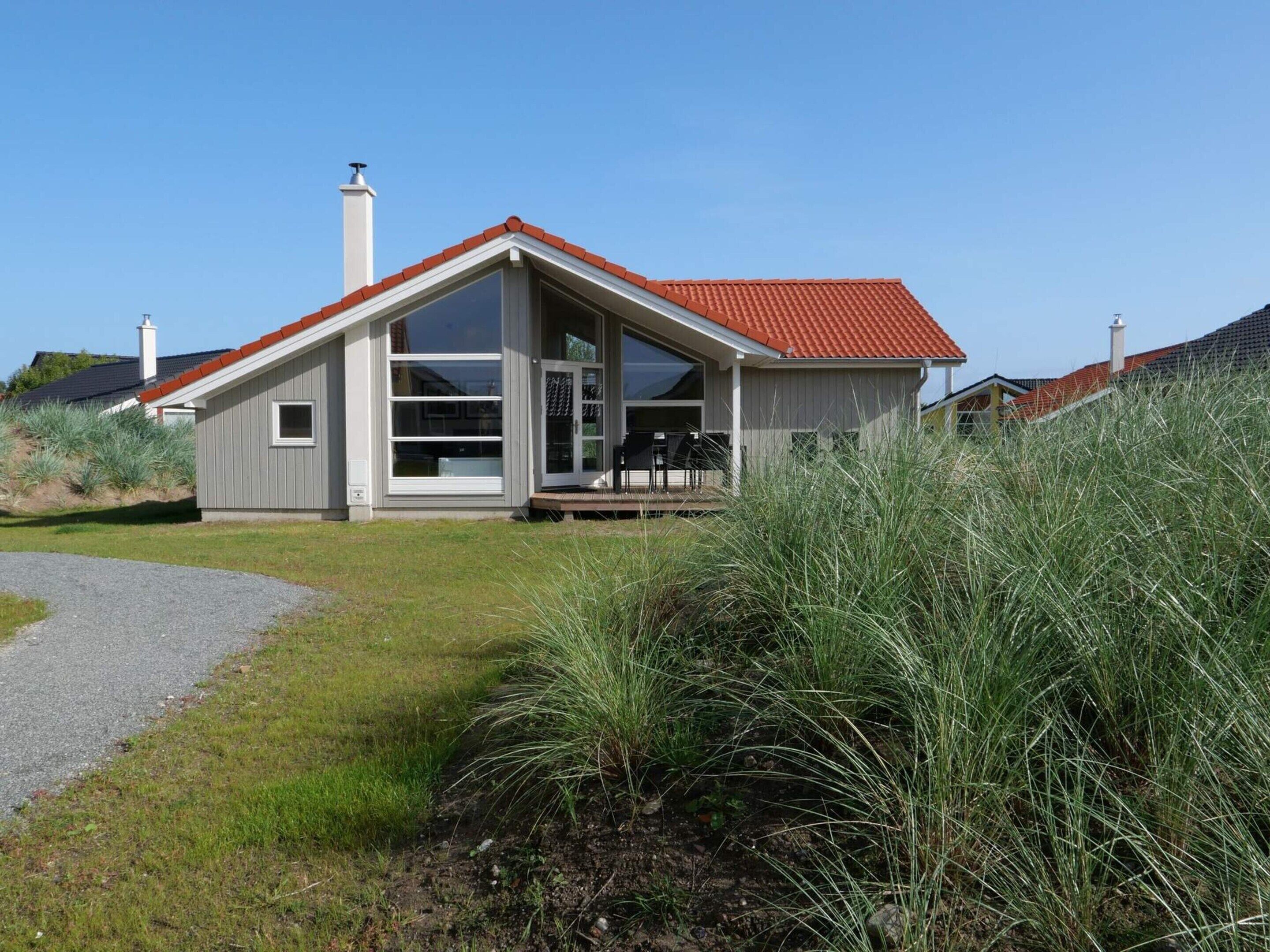 Een modern huis met een rood dak, grote ramen en een overdekte veranda.