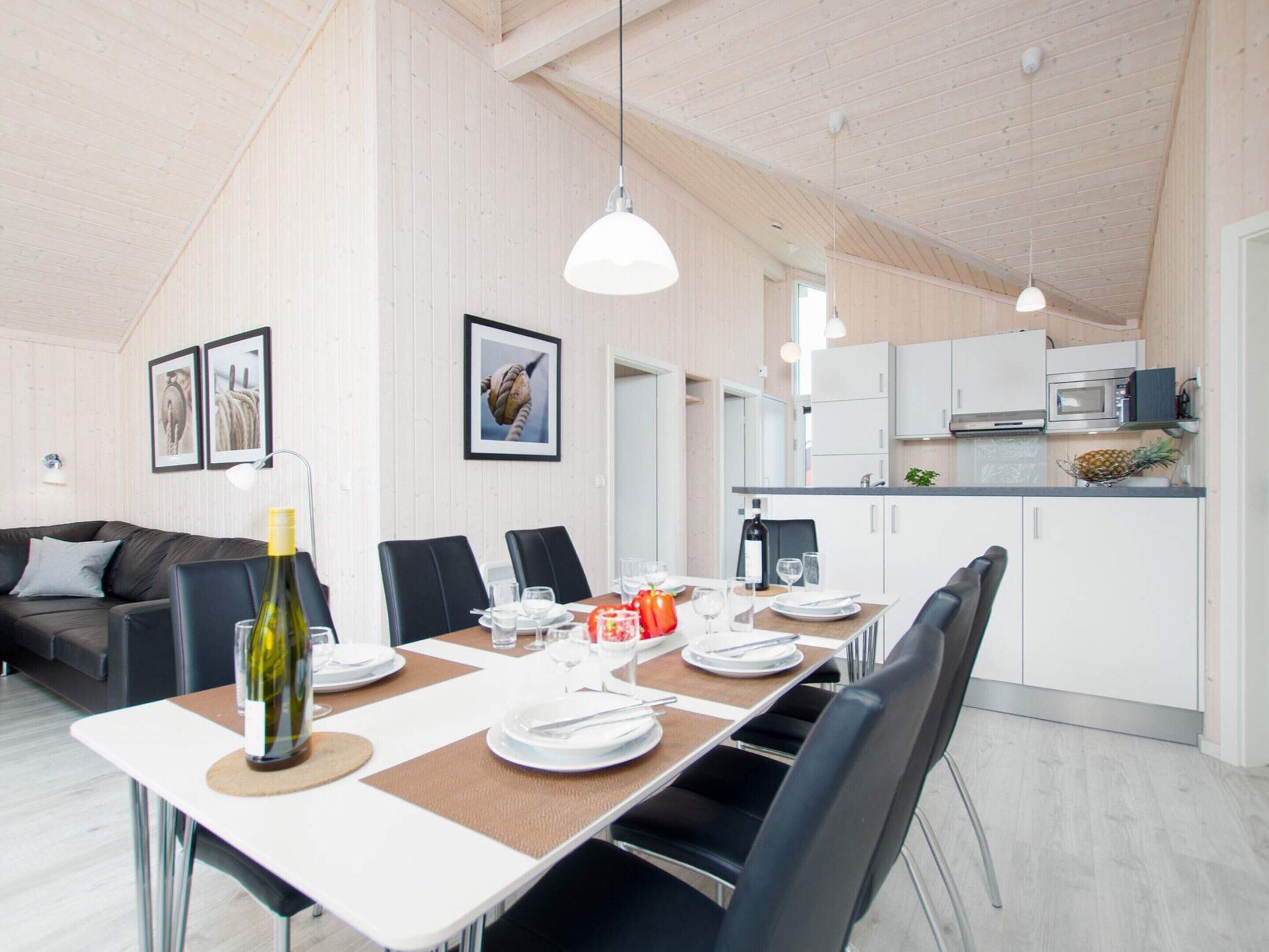 A dining area with a table set for four, kitchen cabinets, a microwave, and a refrigerator in the background.