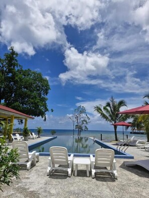 A pool area with lounge chairs, a glass barrier, and a view of the ocean. - Cahaya Asah Resort Tioman Island (Tioman Island)