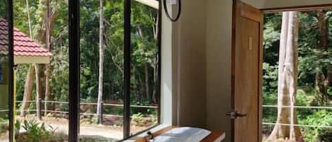 A room with a long table, bar stools, a window with a view of trees, and a door leading outside.