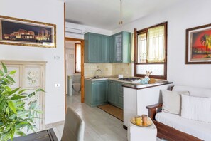 A compact kitchen with teal cabinets, a white countertop, and a dining area with a white sofa and a small table. - Italian Experience - Veranda Sul Conero (Marcelli)