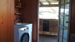 Une buanderie équipée d’un lave-linge, avec des murs en bois et une porte donnant sur un espace extérieur.