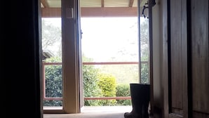 Un hall d’entrée avec un plancher en bois, une plante en pot et une porte donnant sur un espace extérieur avec vue sur la verdure.