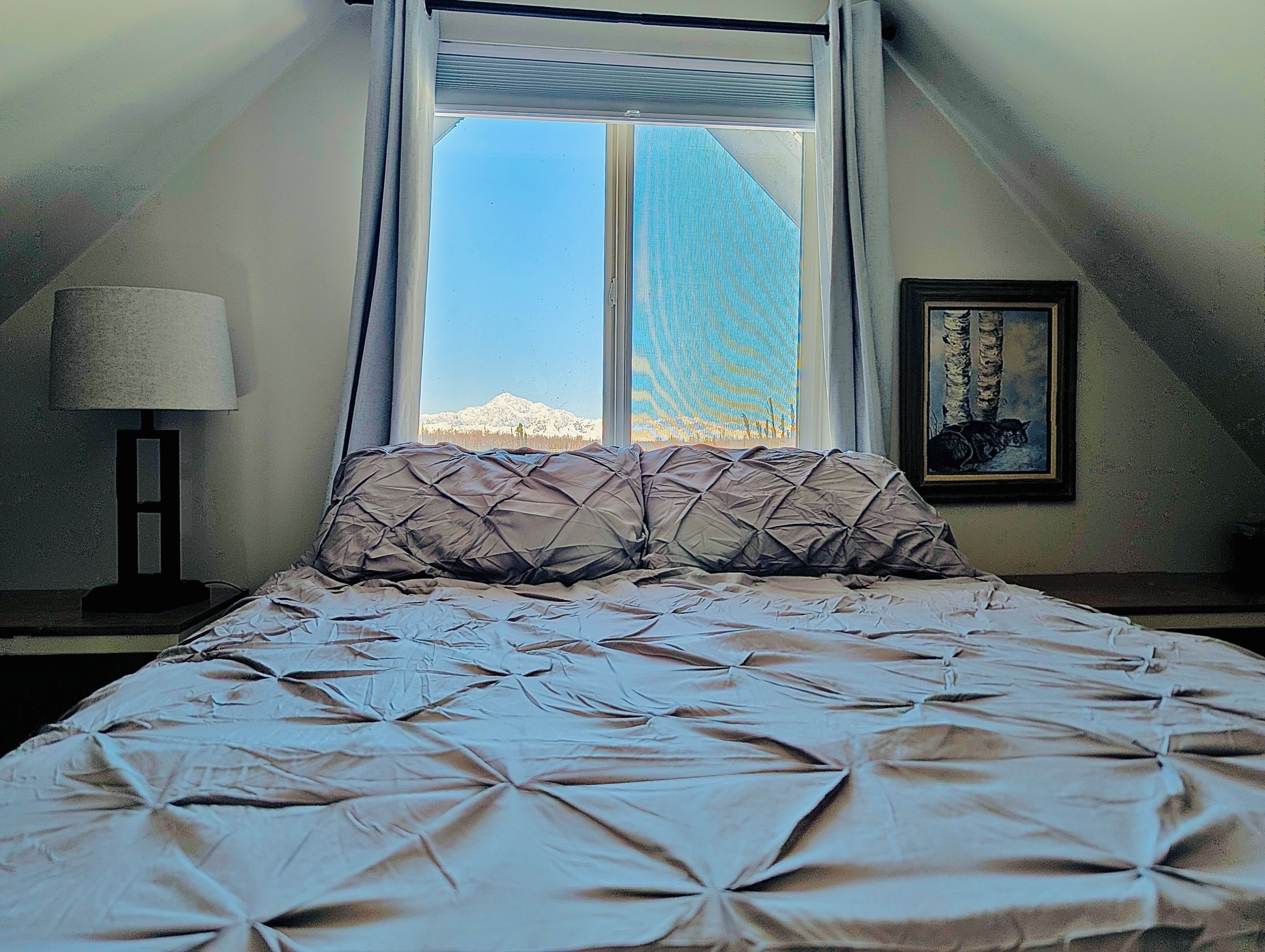 A bedroom with a bed, a window, a lamp, and a painting.