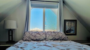 Ein Schlafzimmer mit Bett, Fenster, Lampe und einem Gemälde.