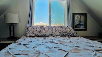 A bedroom with a bed, a window, a lamp, and a painting.