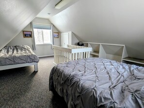 Une chambre avec deux lits, un berceau blanc, une fenêtre et un ventilateur de plafond.