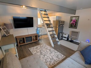Un salon comprenant un téléviseur, un meuble de rangement en bois, un tapis à motifs, un canapé et un escalier.