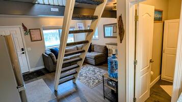 A staircase with a 'Please find your head' sign, a living room with a sofa, a water dispenser, and a door leading to another room.
