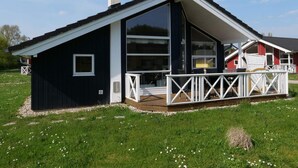 Een modern huis met een groot raam, een balkon met witte hekwerk en een schoorsteen.