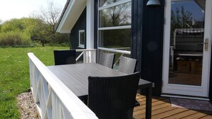 Een terras met een tafel en stoelen, een schuifdeur en uitzicht op de omliggende begroeiing.