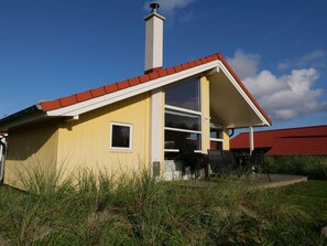 A yellow building with a red roof, a chimney, and a large window.