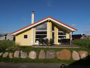 A yellow building with a red roof, a chimney, and a covered patio with chairs.