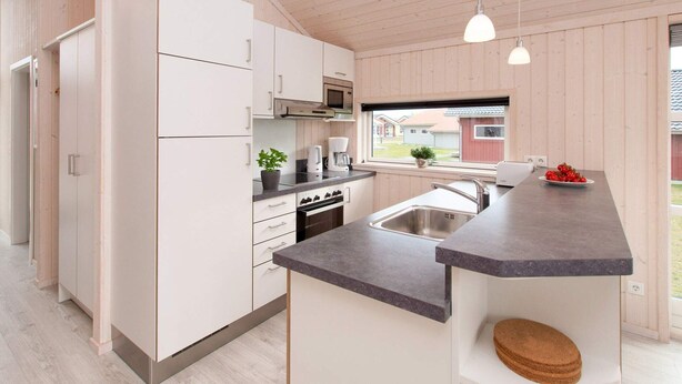 A modern kitchen with white cabinets, a granite countertop, a built-in oven, and a window overlooking a yard.