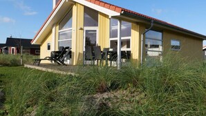 A yellow building with a red roof, large windows, and outdoor seating.