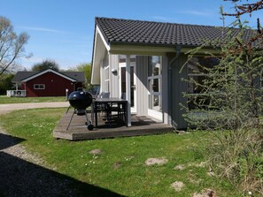 Ein Haus mit überdachter Terrasse, einem Grill und einem kleinen Schuppen im Hintergrund.