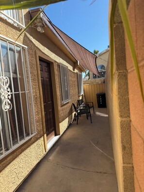 A house with a textured exterior, a brown door, barred windows, and a patio area with chairs. - Soothing 1-bedroom apartment with AC in vibrant Las Vegas (Las Vegas)