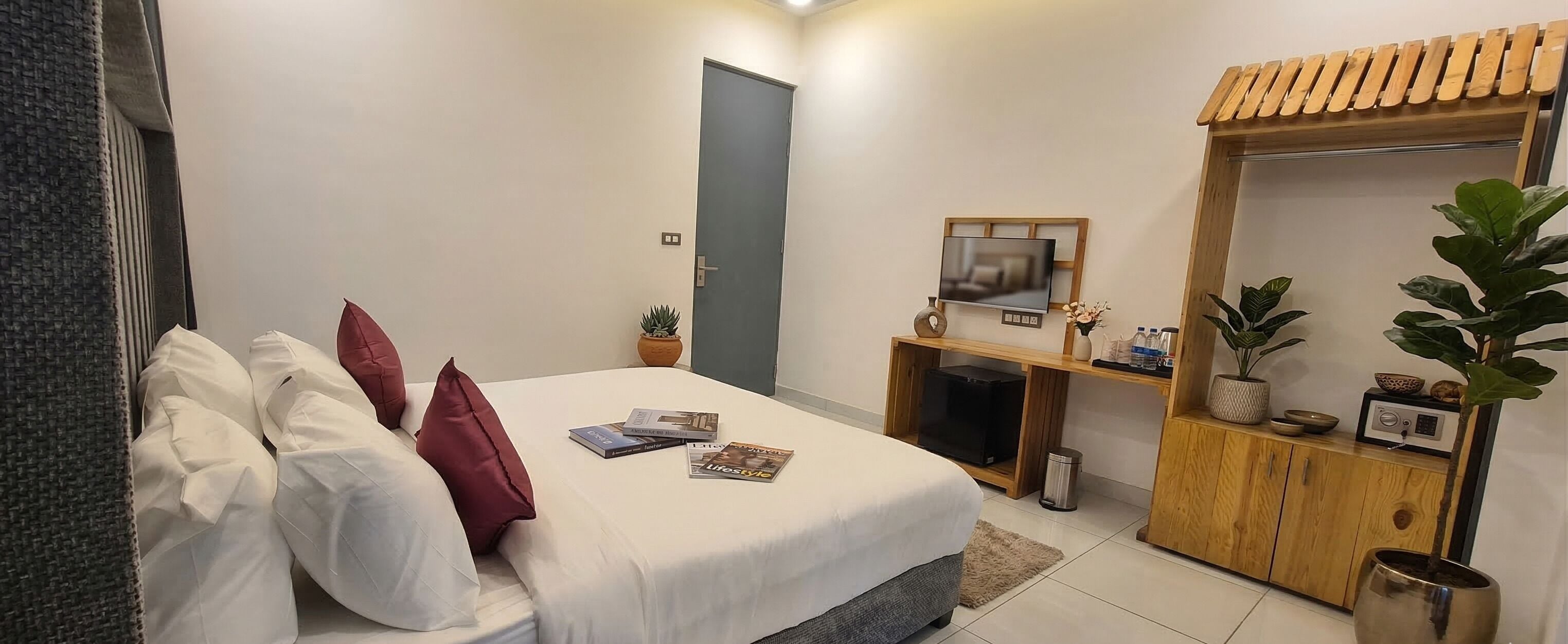 A bedroom with a bed, a TV, a wooden cabinet, and a potted plant.