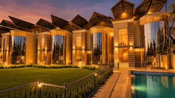 A modern hotel with a swimming pool, large windows, and a well-lit exterior.