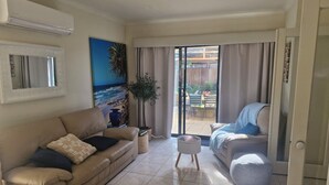 A living room with a beige sofa, a coffee table, a potted plant, and a sliding glass door leading to an outdoor area with chairs and a table. - Beautiful family home ,fully furnished in Bendigo over Easter 3rd April  to 8th (Strathdale)