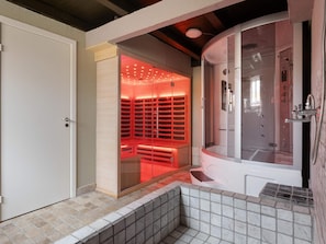 A modern bathroom with a walk-in shower, a glass-enclosed sauna, and a tiled floor.
