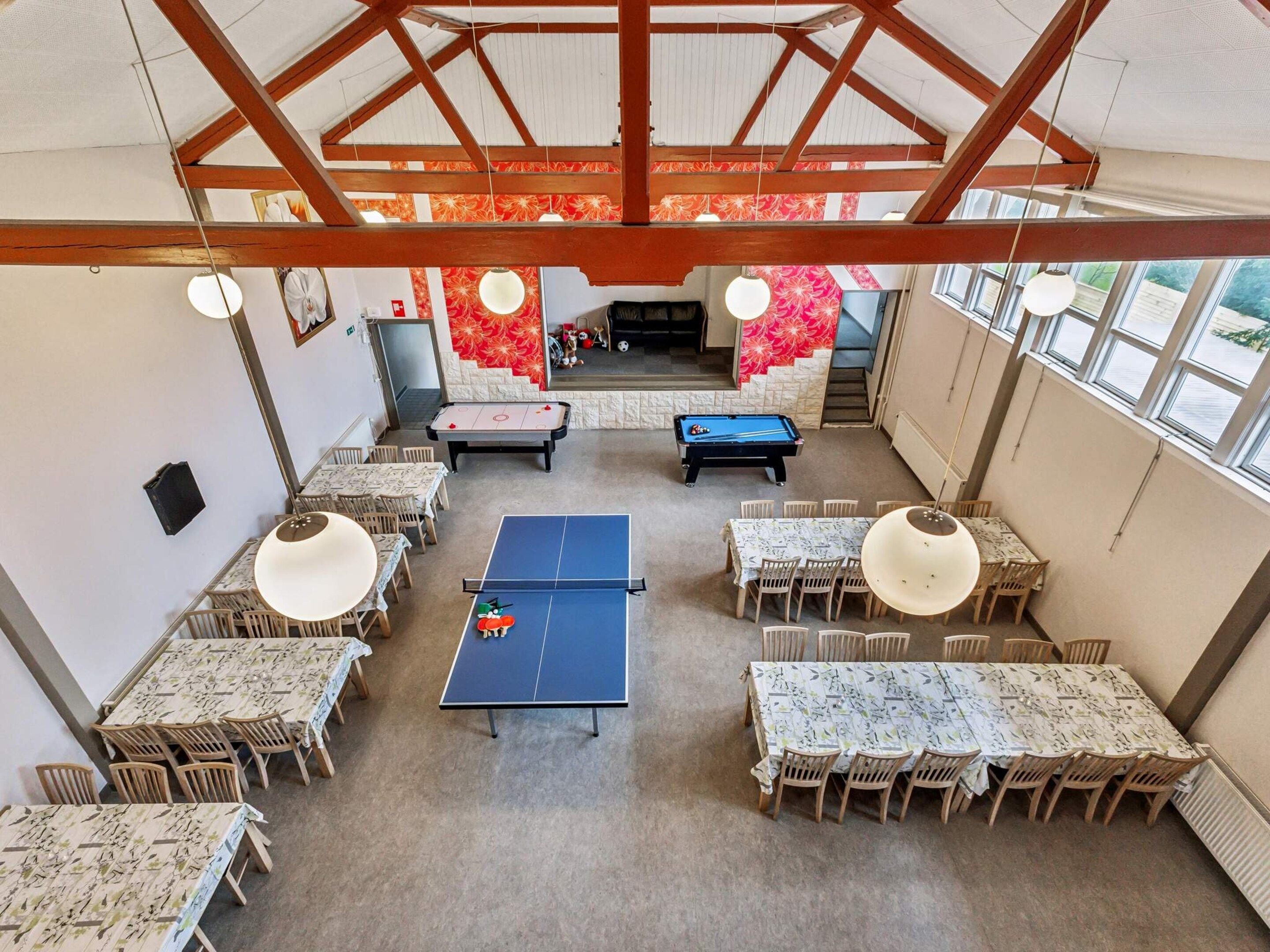 A spacious indoor area with multiple tables and chairs, a ping pong table, and two pool tables.
