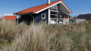 Una casa de una sola planta con techo de tejas rojas, una chimenea y barandilla de balcón blanca.