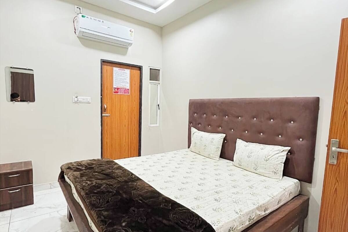 Un dormitorio con una cama, ventilador de techo, equipo de aire acondicionado, puerta de madera y un mueble pequeño.
