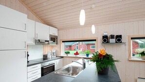 Ett modernt kök med vita skåp, en svart bänkskiva, en diskho i rostfritt stål, en inbyggd ugn, en mikrovågsugn och ett fönster med utsikt över en röd byggnad.